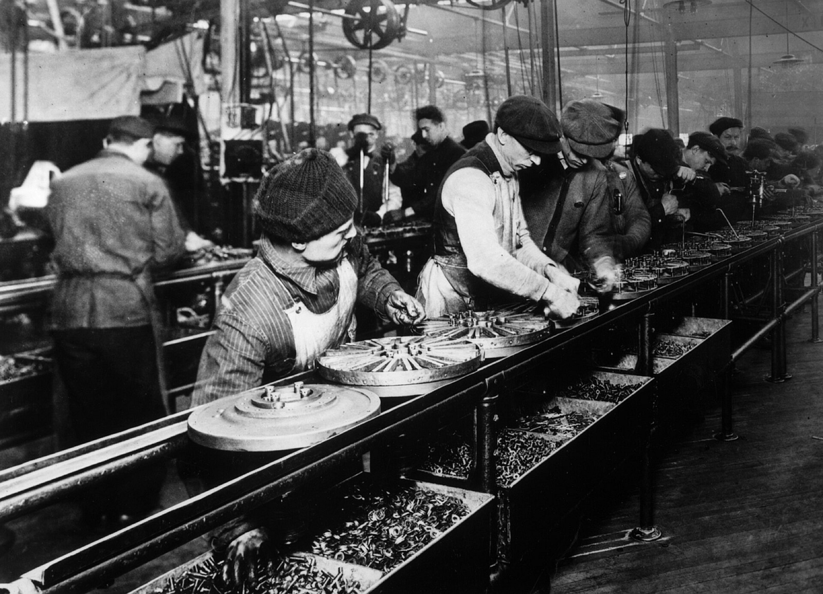 Operários trabalham lado a lado em uma linha de montagem, exemplificando o ritmo e a organização industrial da produção em série.