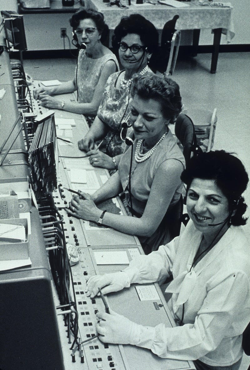 Operadoras trabalham em uma central telefônica com cabos e painéis, em serviço contínuo.
